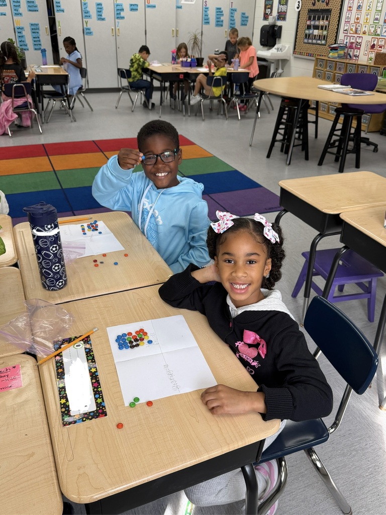 Two students sitting in a classroom, counting M&Ms and writing numbers on a paper.