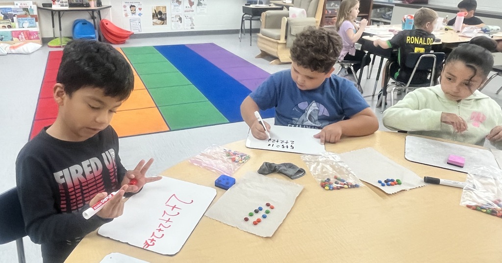 Two students sitting in a classroom, counting M&Ms and writing numbers on a whiteboard.