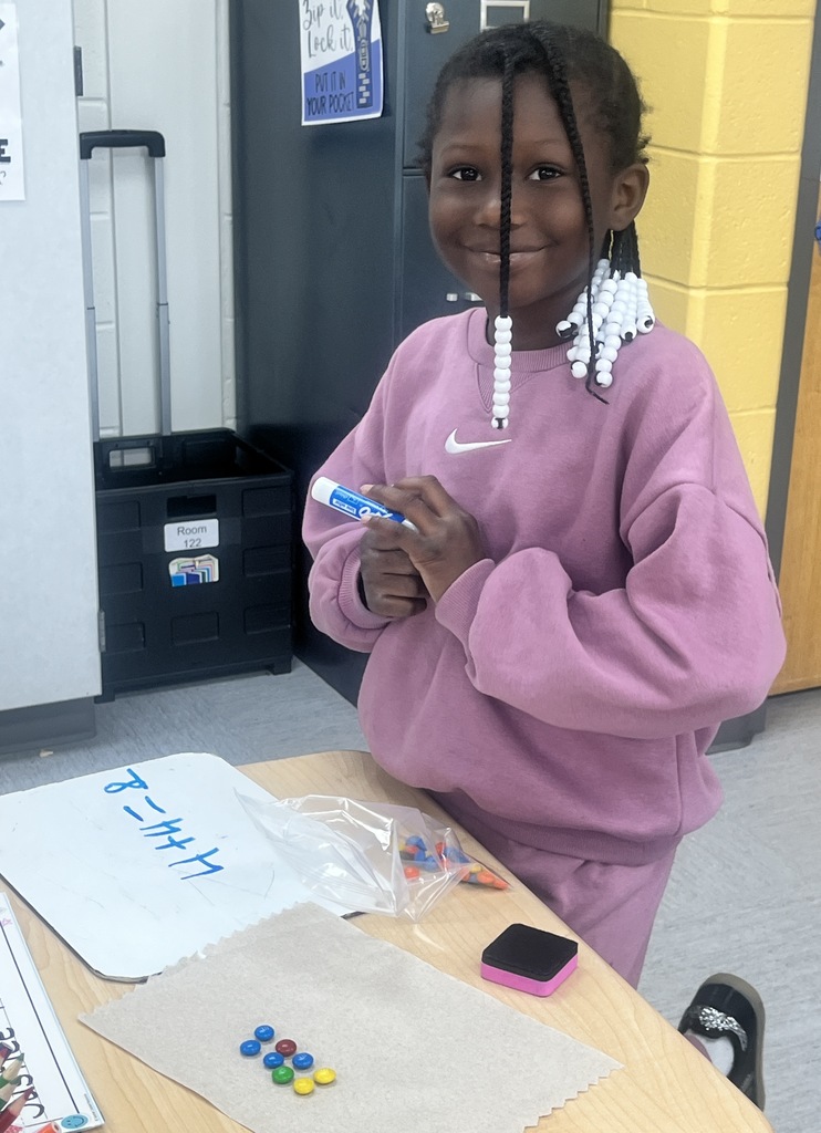 A student sitting in a classroom, counting M&Ms and writing numbers on a whiteboard.