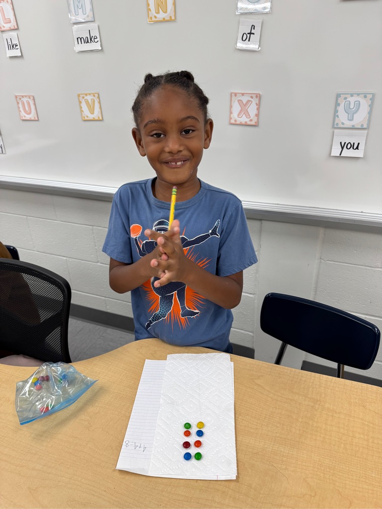 A student sitting in a classroom, counting M&Ms and writing numbers on a paper.