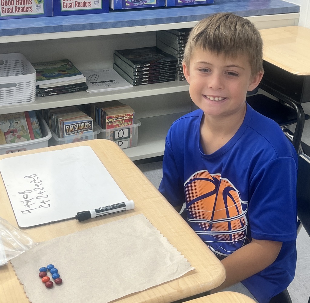 A student sitting in a classroom, counting M&Ms and writing numbers on a whiteboard.