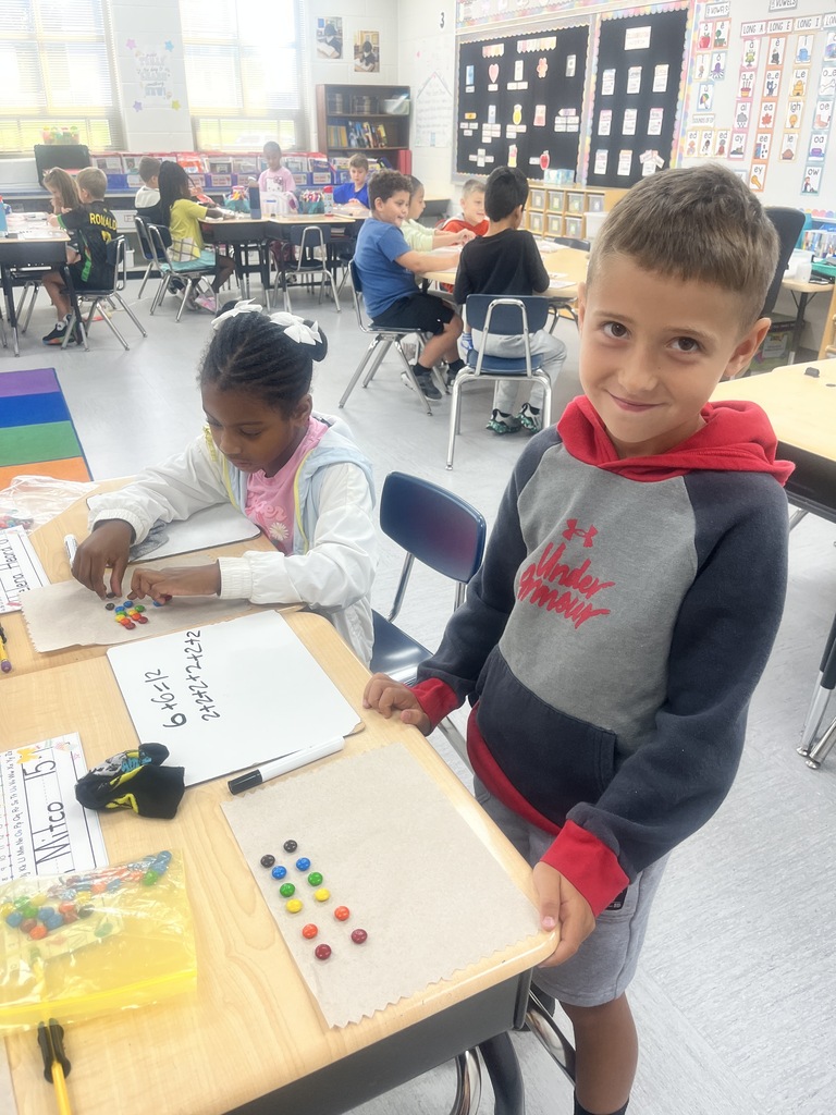 Two students sitting in a classroom, counting M&Ms and writing numbers on a whiteboard.