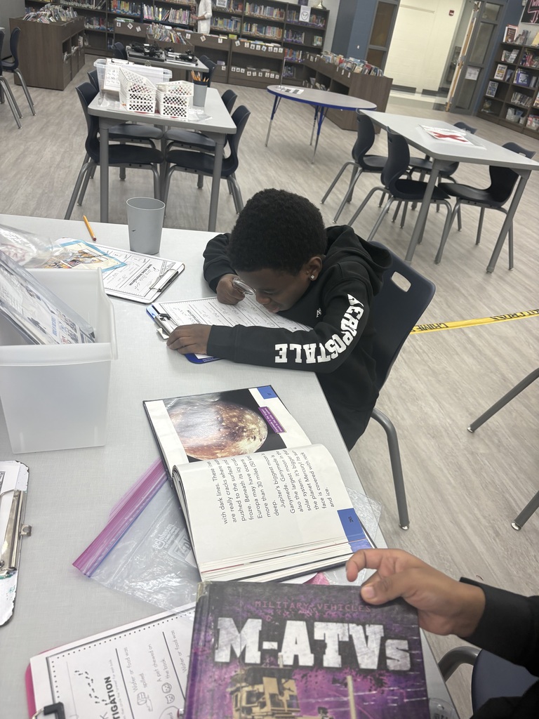 A student looking through a magnifying glass at a book.