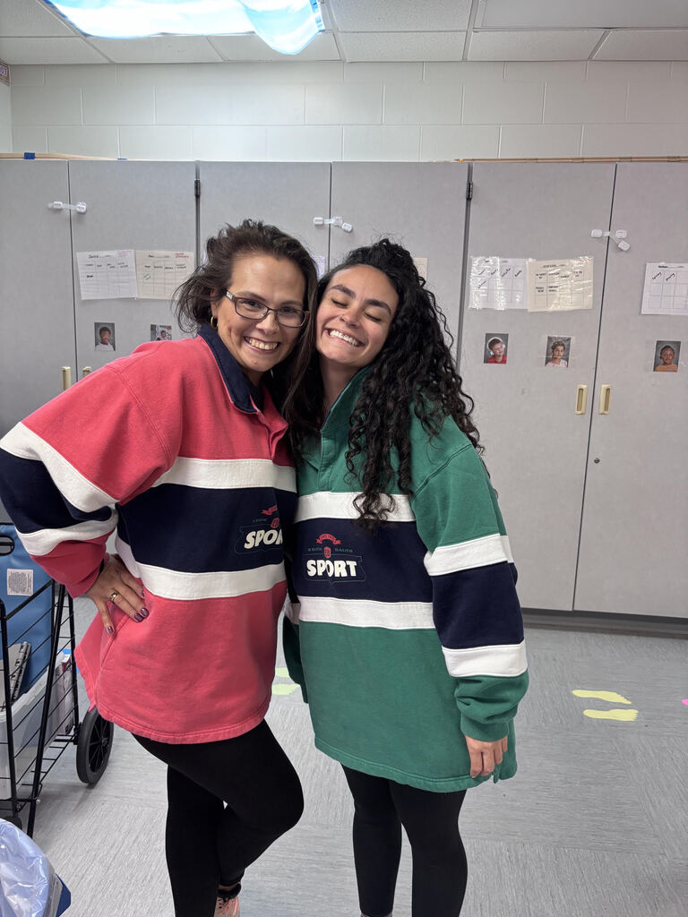 Two teachers wearing green and red jerseys smiling in a classroom.