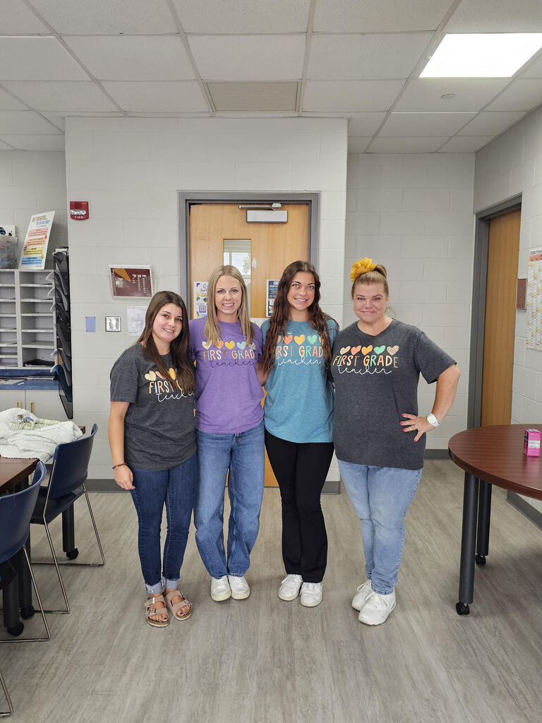 Four teachers with 1st grade tshirts standing in a row smiling.