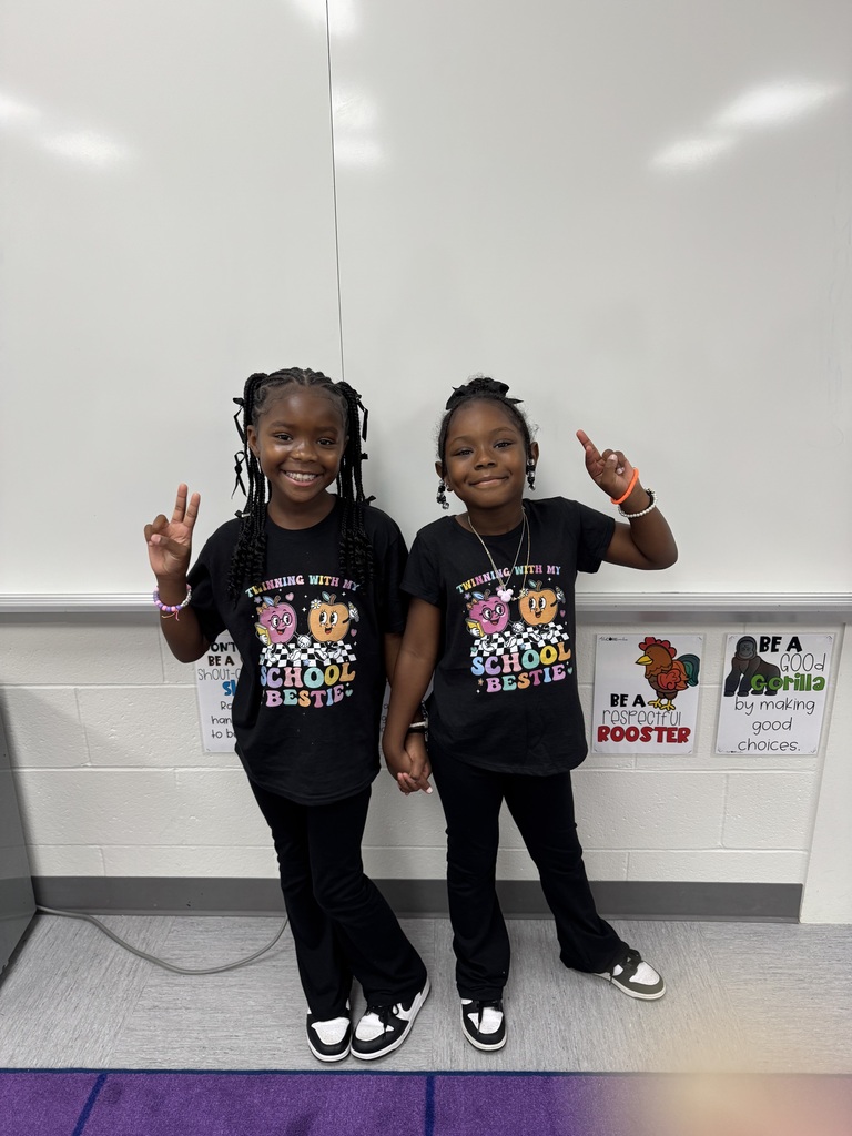 Two students wearing black tshirts and pants smiling in a classroom.