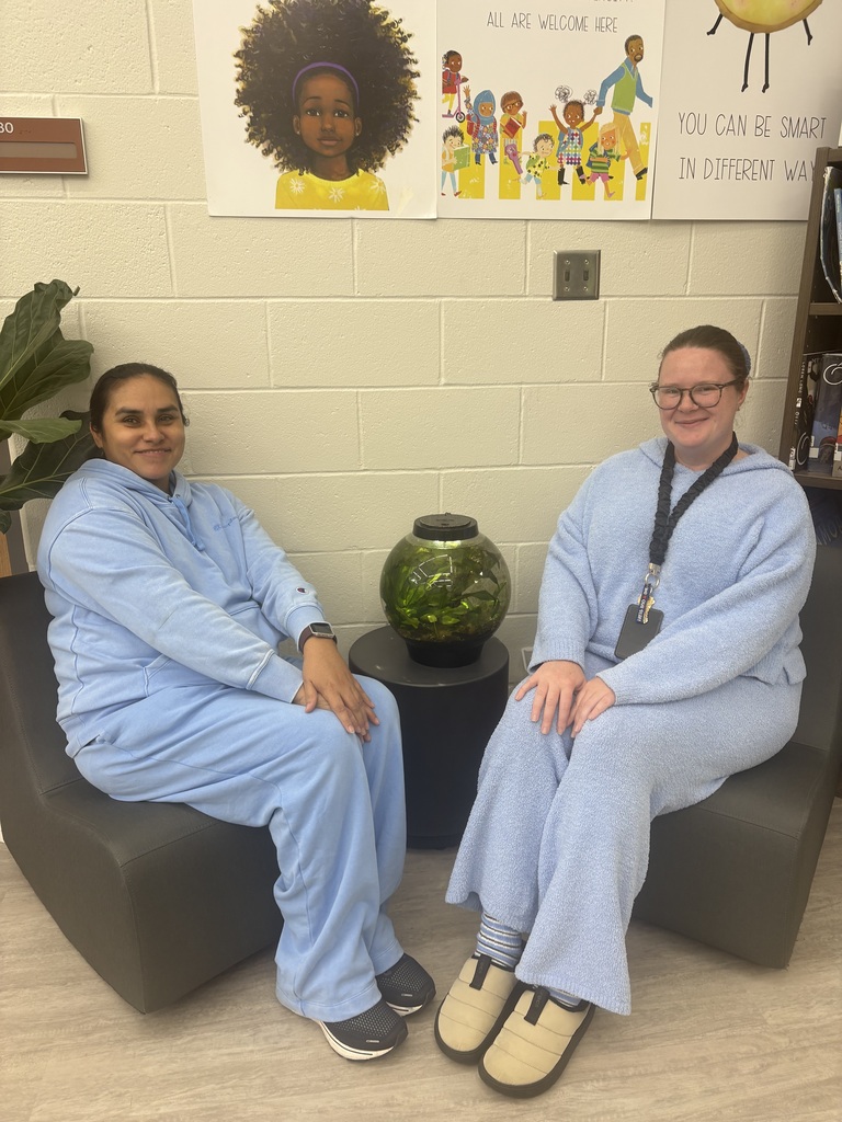 Two teachers wearing blue  sitting in a library by a fish tank.