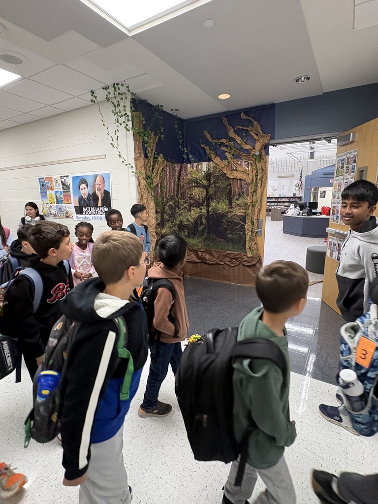 Students in a hallway in an elementary school looking at the entrance to the library that is decorated like a forest.