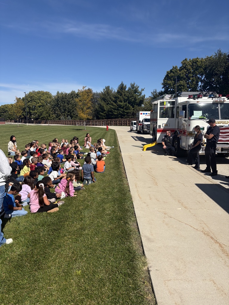 Wallin Oaks ES students sit on grass outside learning about fire safety. Firetruck in the background