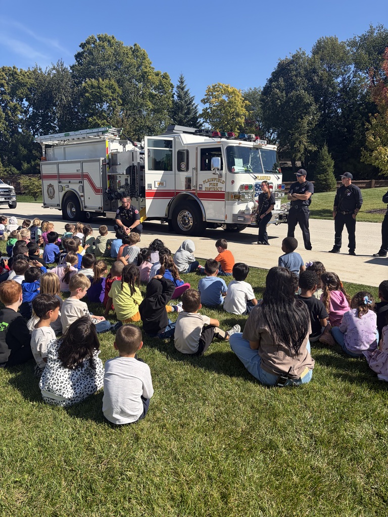 Wallin Oaks ES students sit on grass outside learning about fire safety. Firetruck in the background