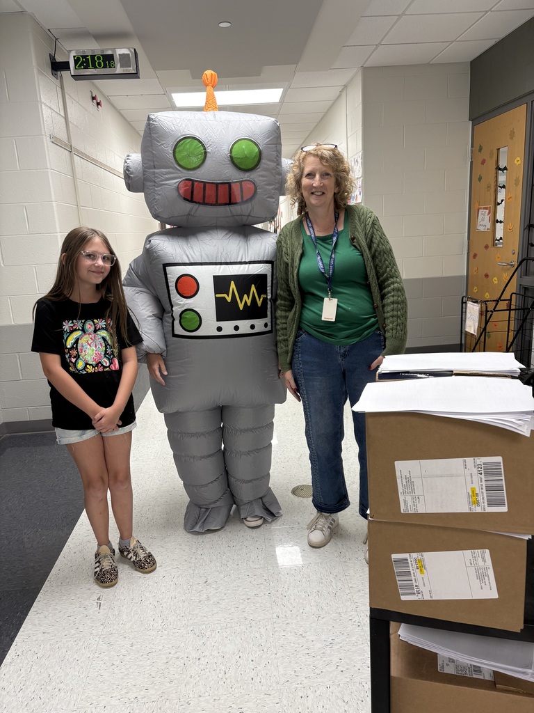 A student and teacher standing in a school hallway with another teacher in a robot costume.