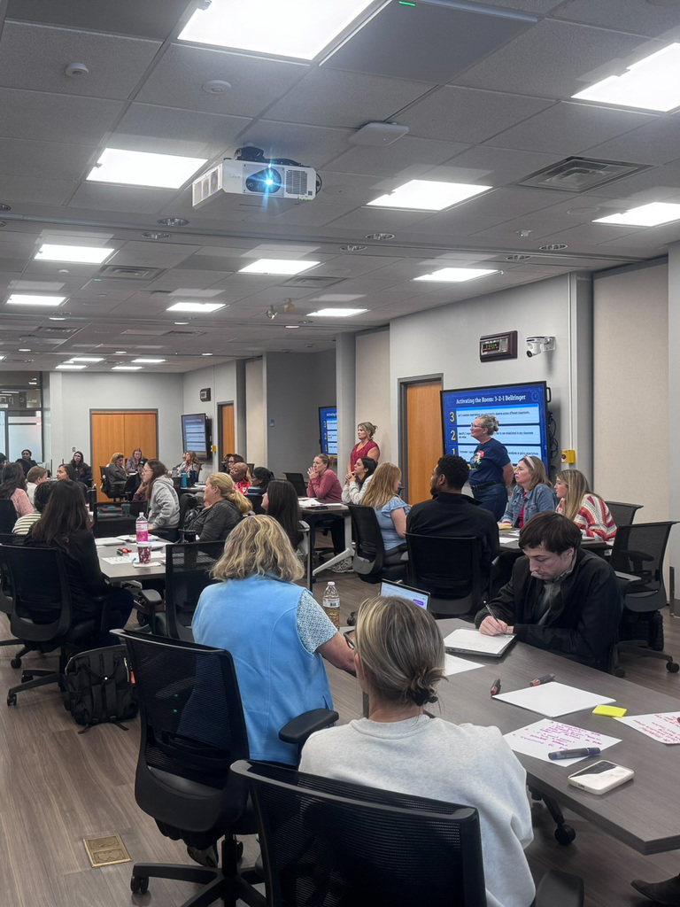 group of adults in room sitting at tables writing