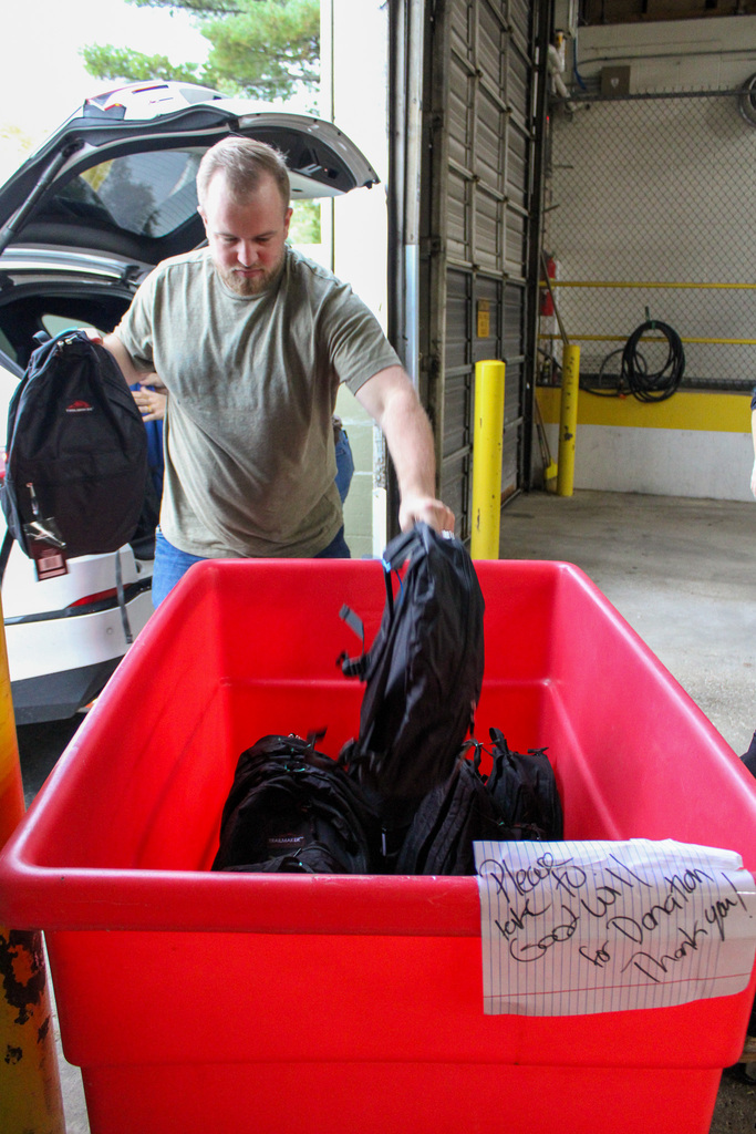 man putting backpacks in a red bin