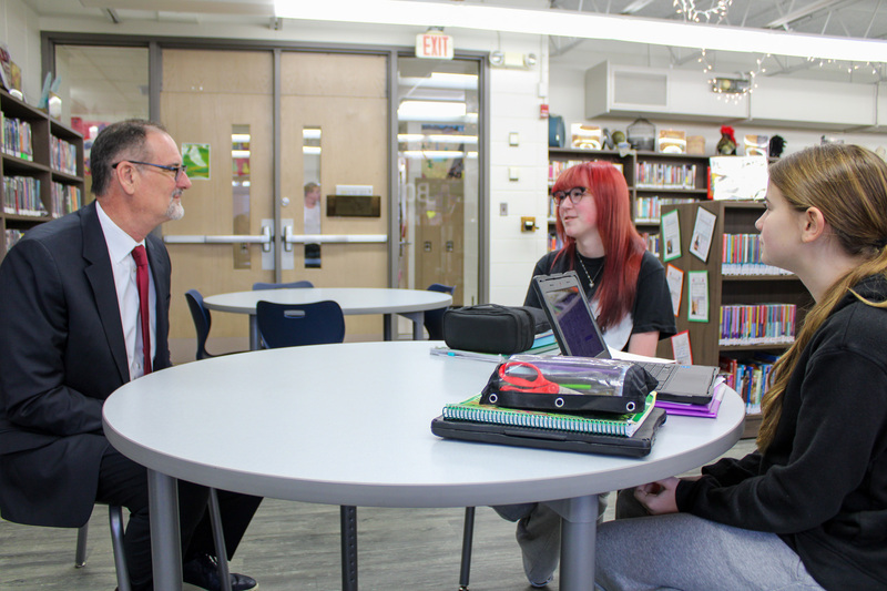 Adult in suit sits for interview with two middle school students 