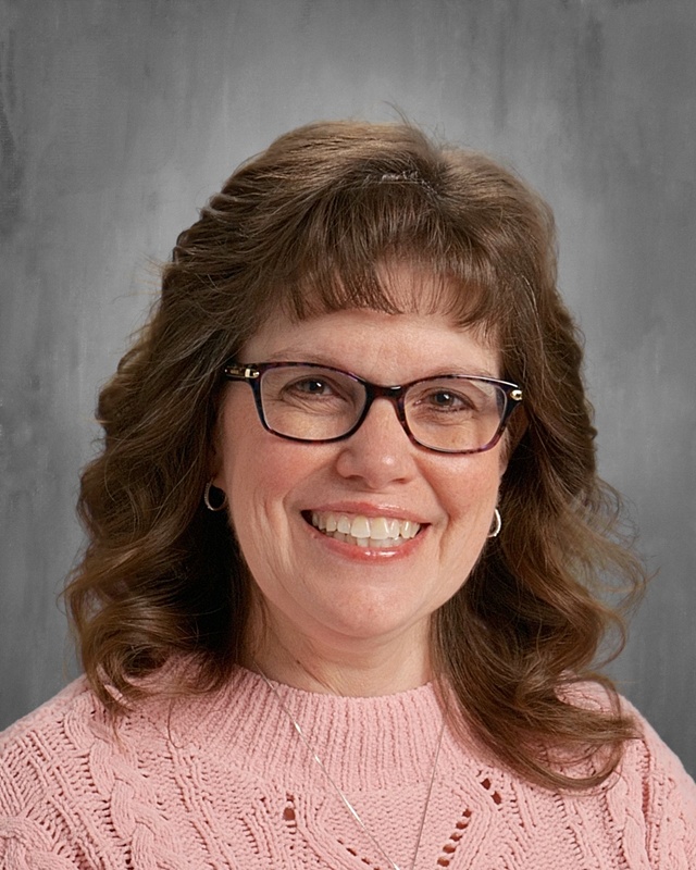 woman with shoulder length bronw hair, glasses, wearing a pink sweater