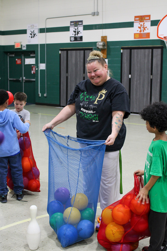 physical education teacher holds open blue bag so students can put foam balls inside