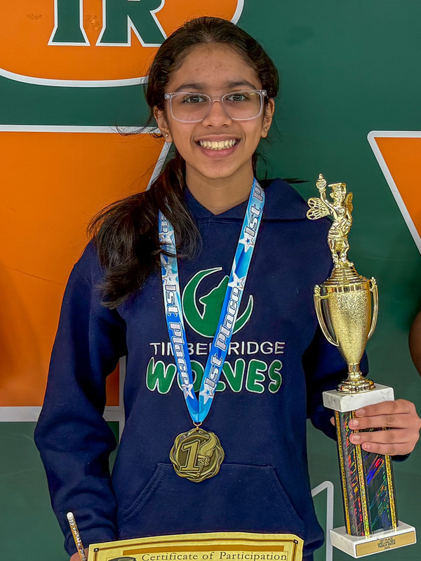 student wearing blue sweatshirt and glasses with medal around neck and holding trophy