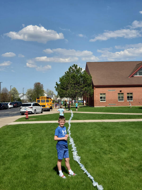 Student stands outside elementary school next to long line of plastic bags tied together