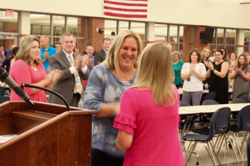 Ann Mennonno shakes hands with School Board President Jessica Elston, while her peers give her a standing ovation