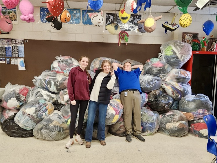 picture of two students and a teacher with piles of donated clothes