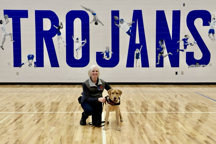 picture of Jean (handler) and Ginny (therapy and safety dog) in front of Trojans sign at the field house 