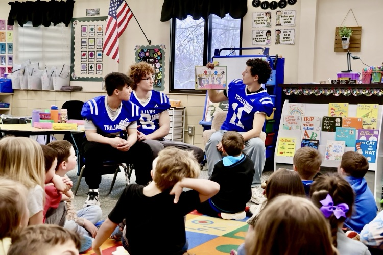 three football players reading to a classroom of elementary students for reading month