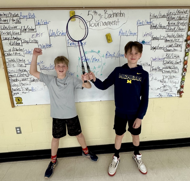 picture of two students holding badminton rackets in front of a whiteboard with a badminton bracket written out 