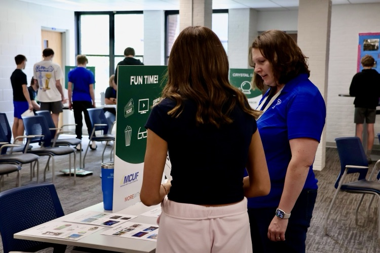 picture of a student with a staff member helping them at a station at a reality fair 
