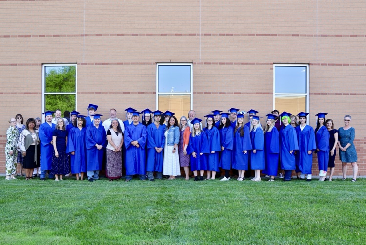 group picture of RHS graduates in their cap and gowns with various RHS staff members outside the performing arts center