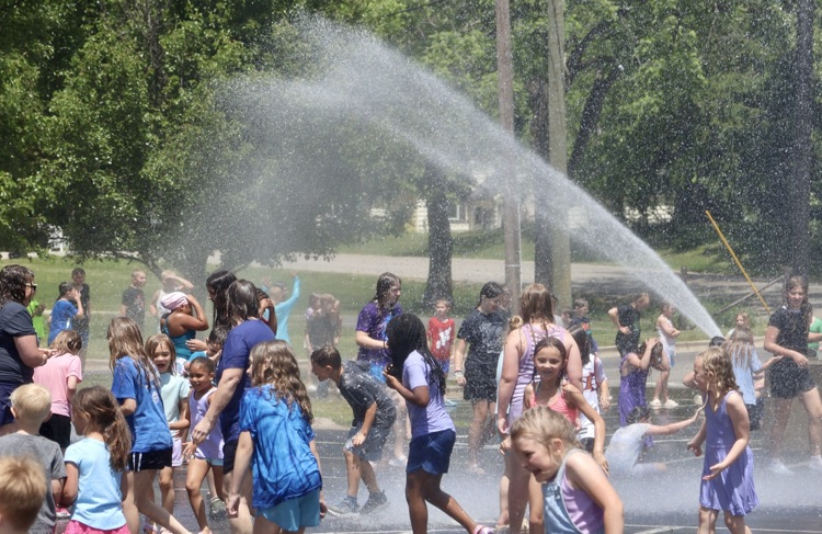 picture of cooper students playing and running while being sprayed by a hose for their fire truck cool off