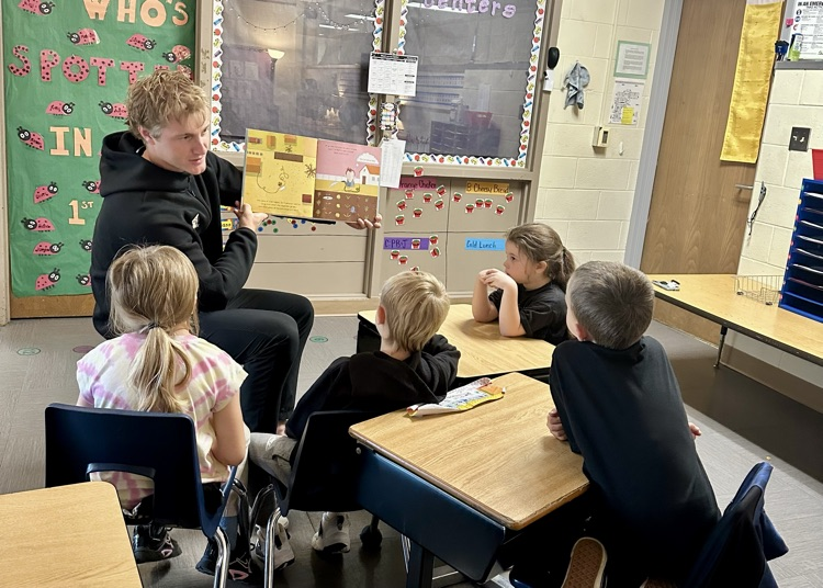 picture of Kalamazoo college soccer player reading to a group of elementary students