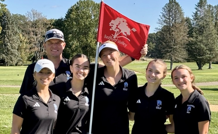 picture of the girls varsity golf team with their coach standing by a Bedford valley golf flag