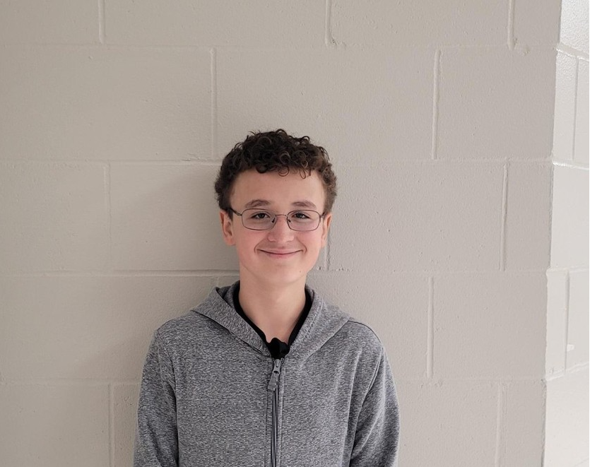 male student with brown hair , glasses and a grey hoodie