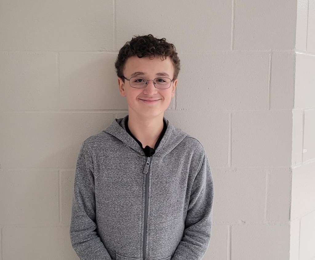 male student with brown hair, curly glasses and a grey hoodie