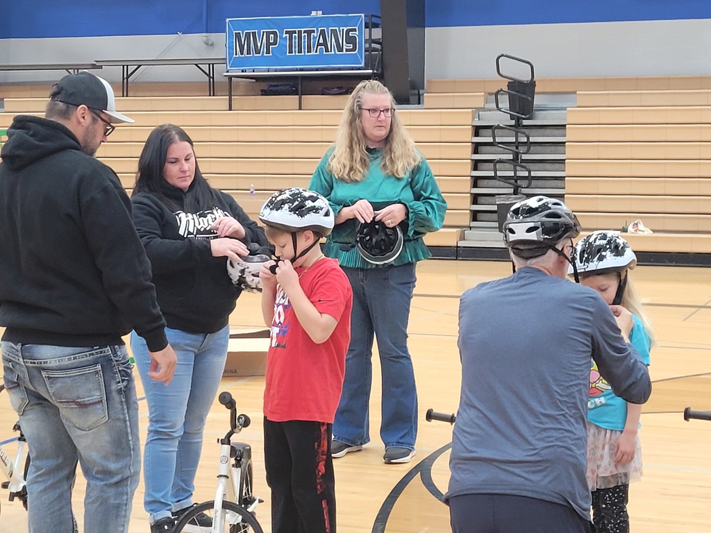 female adult helping students with putting bike helmets on