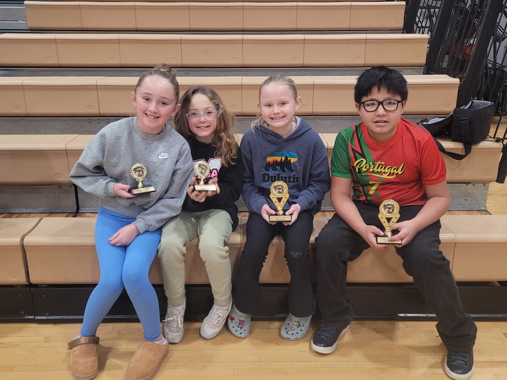 4 students who are sitting on the bleachers with their spelling bee trophies