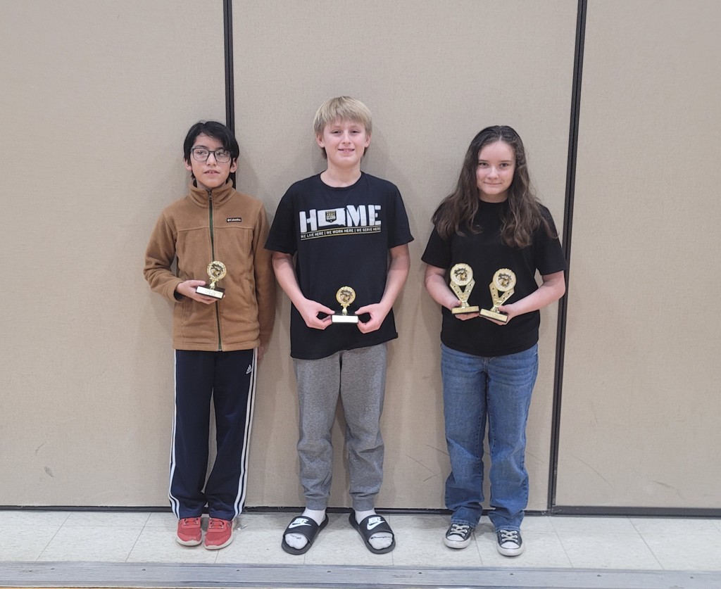 two male students and one female 6th grade students posing with their spelling bee trophies