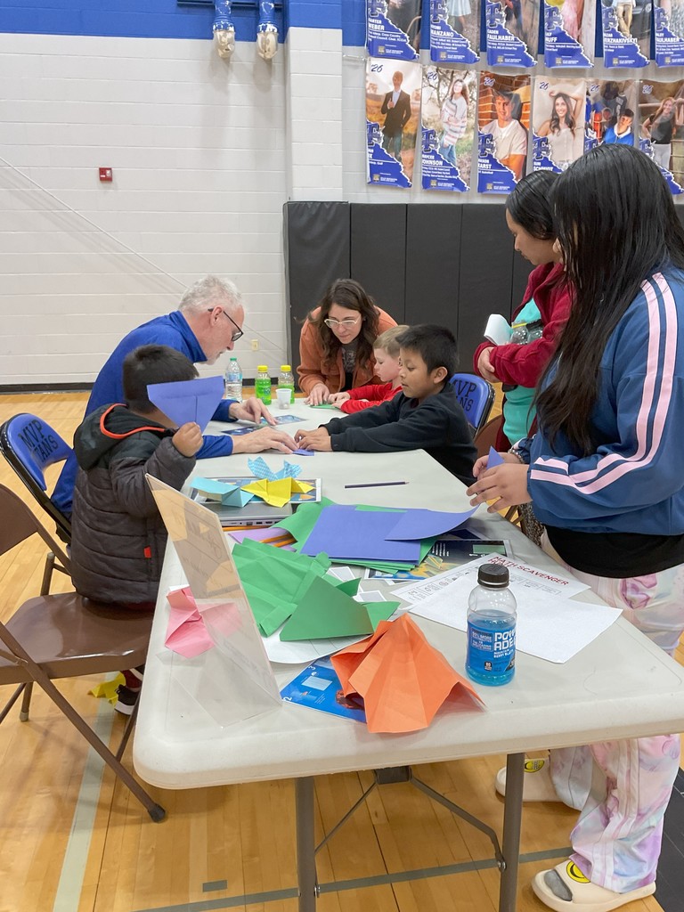 a group of students and a staff member creating paper airplanes 