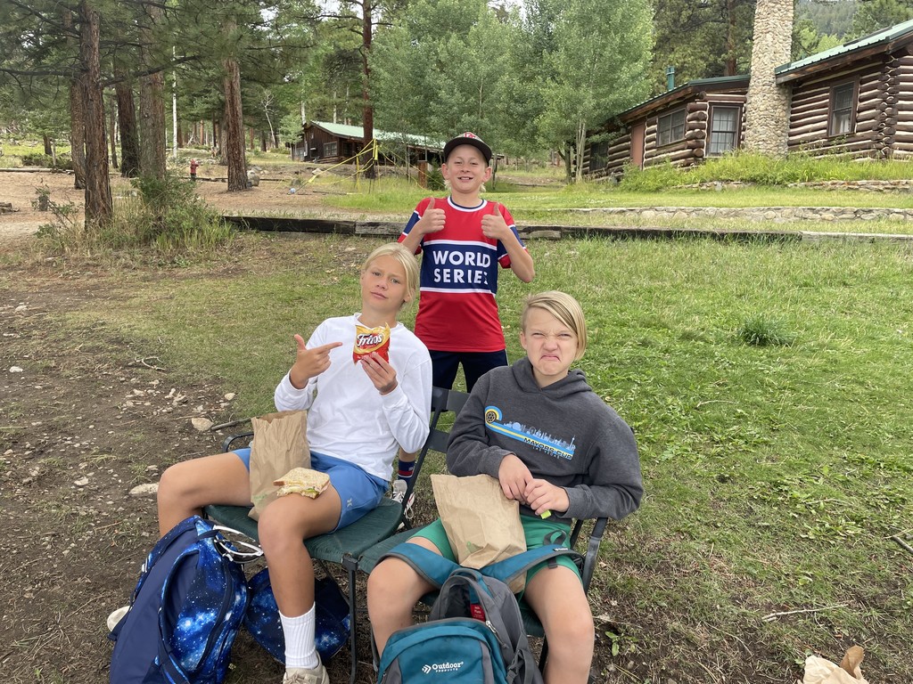 3 kids outside cabins enjoying lunch