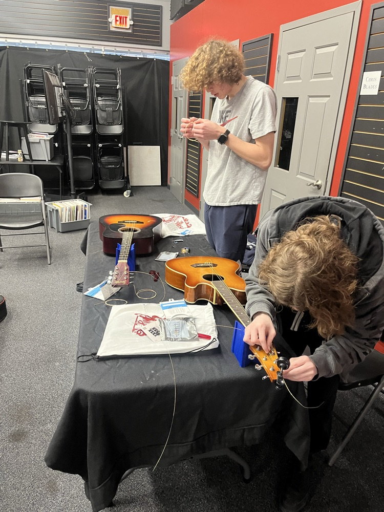 Guitar students practicing stringing an acoustic guitar
