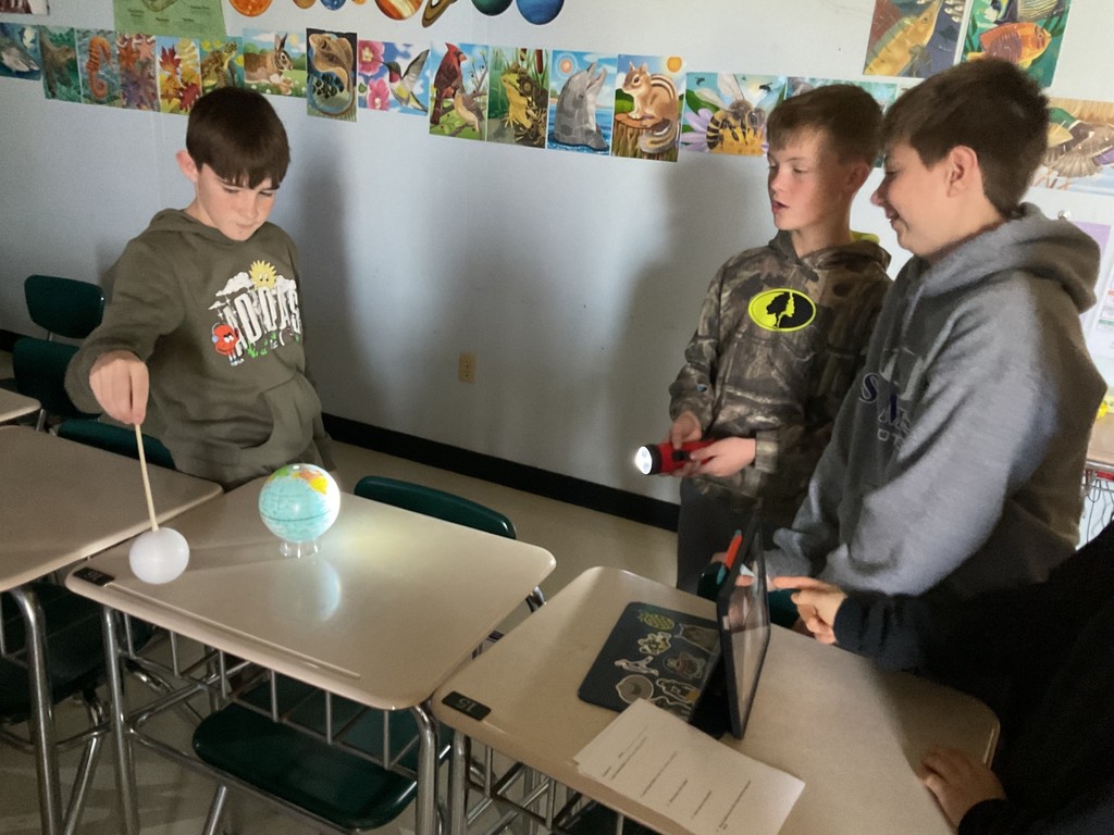 Sixth grade science students use globes, styrofoam balls, and flashlights to model solar and lunar eclipses, demonstrating how the Sun, Earth, and Moon align to create shadows during an eclipse.