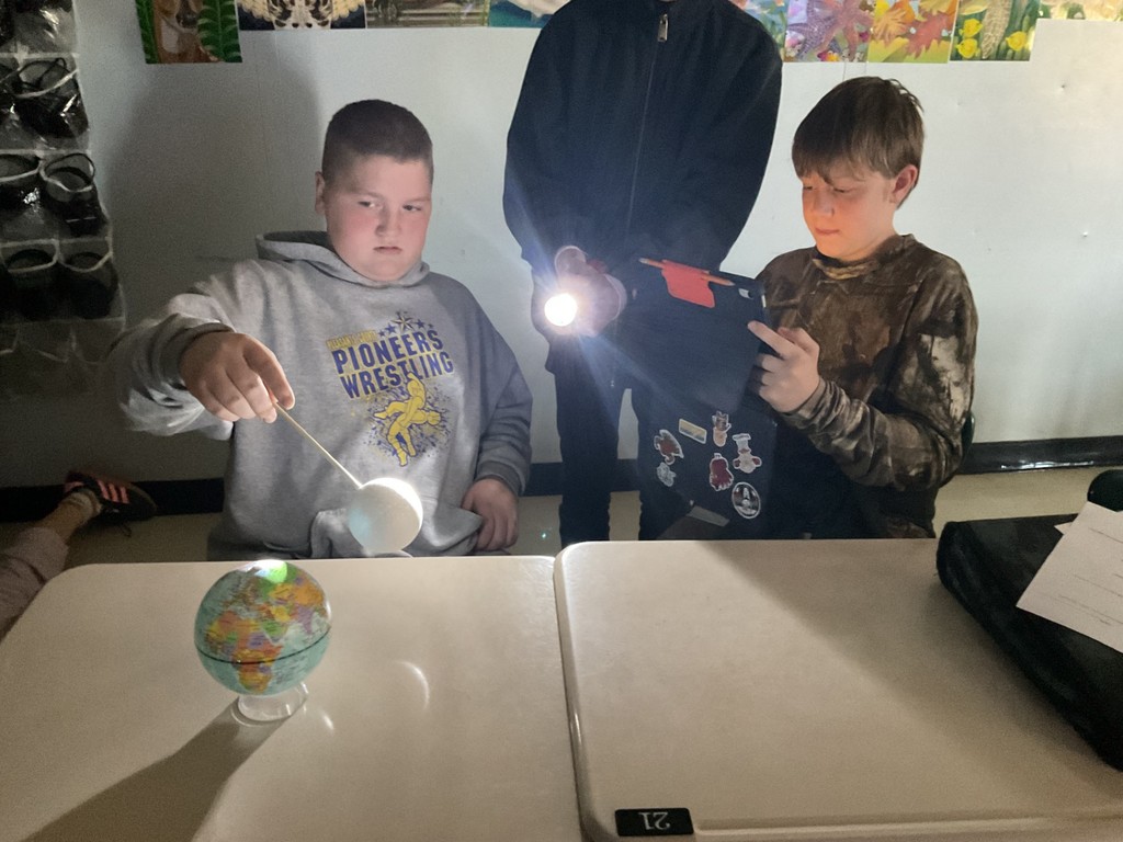 Sixth grade science students use globes, styrofoam balls, and flashlights to model solar and lunar eclipses, demonstrating how the Sun, Earth, and Moon align to create shadows during an eclipse.