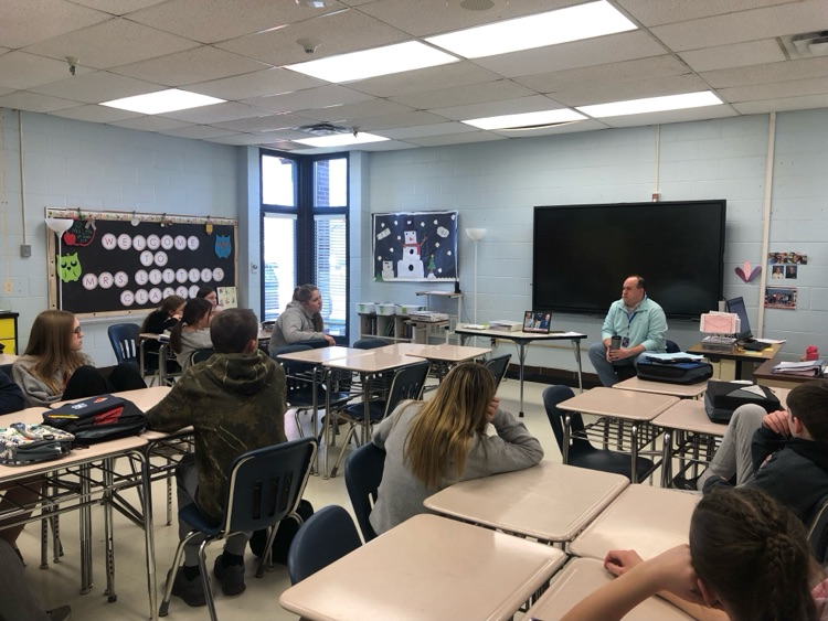 TV and radio play-by-play announcer Eric Little speaks to a middle school journalism class, sharing insights about broadcasting while students listen attentively.