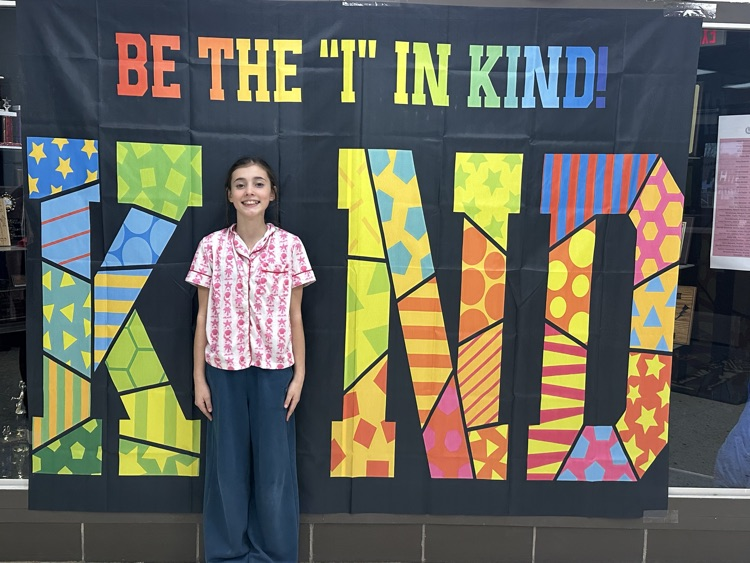 A student standing in front of a banner that says be the I in Kind