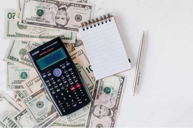 Calculator, money, notepad and pencil.