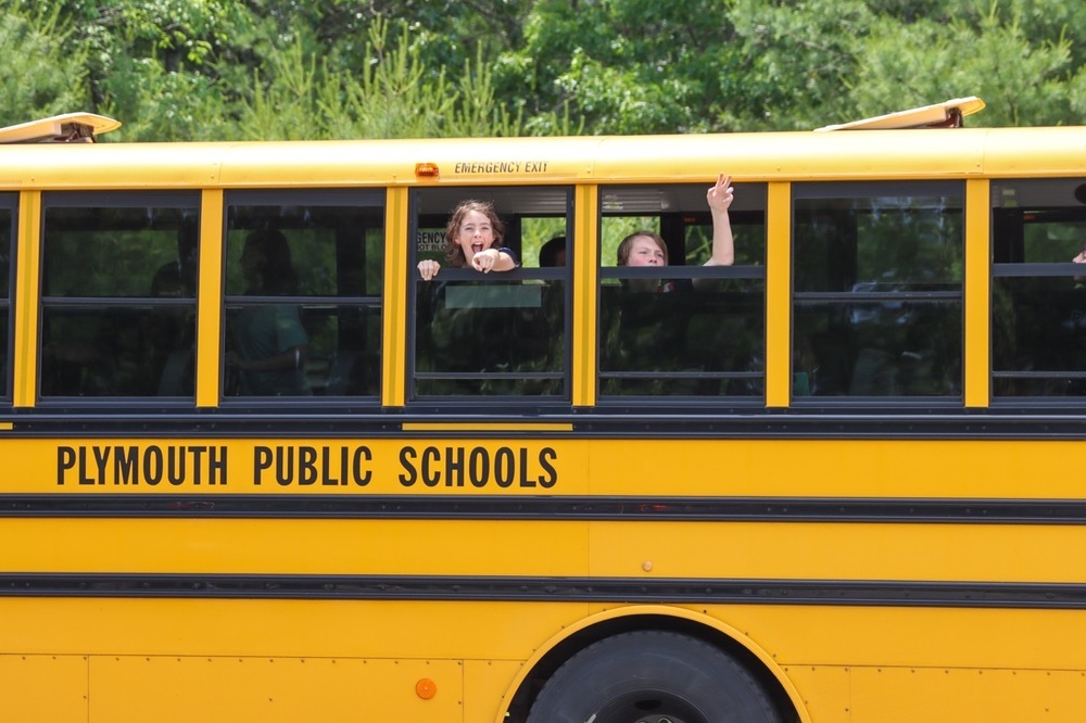 Students smile out the windows of a yellow school bus,