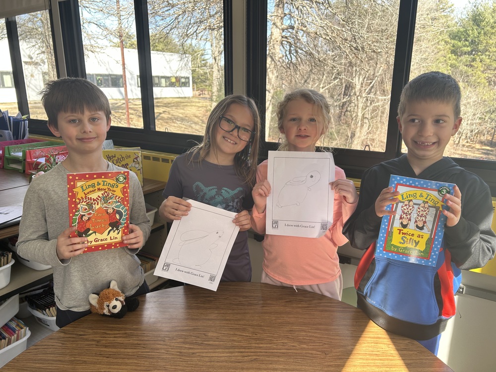 Elementary students holding books and drawings.