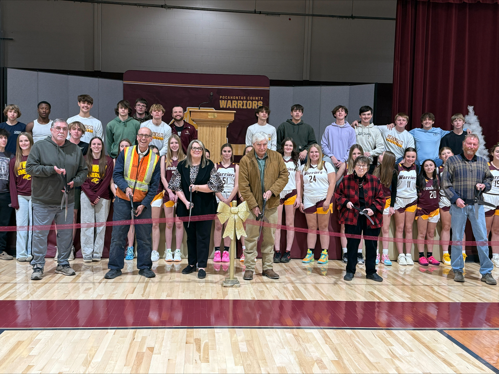 Members of the Pocahontas County BOE curring ribbon on gym floor with students in background