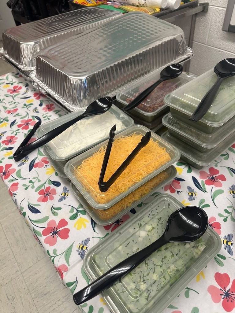 A table displays a lunch setup with covered trays and containers of toppings such as shredded cheese and onions, prepared for staff appreciation.