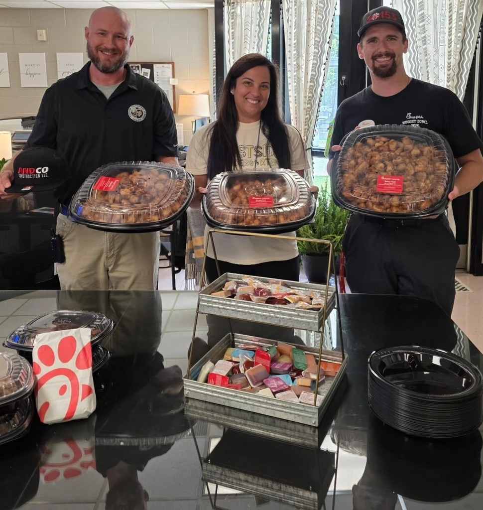 Principal, teacher, and Chic-fil-a employee posing with trays of chicken nuggets